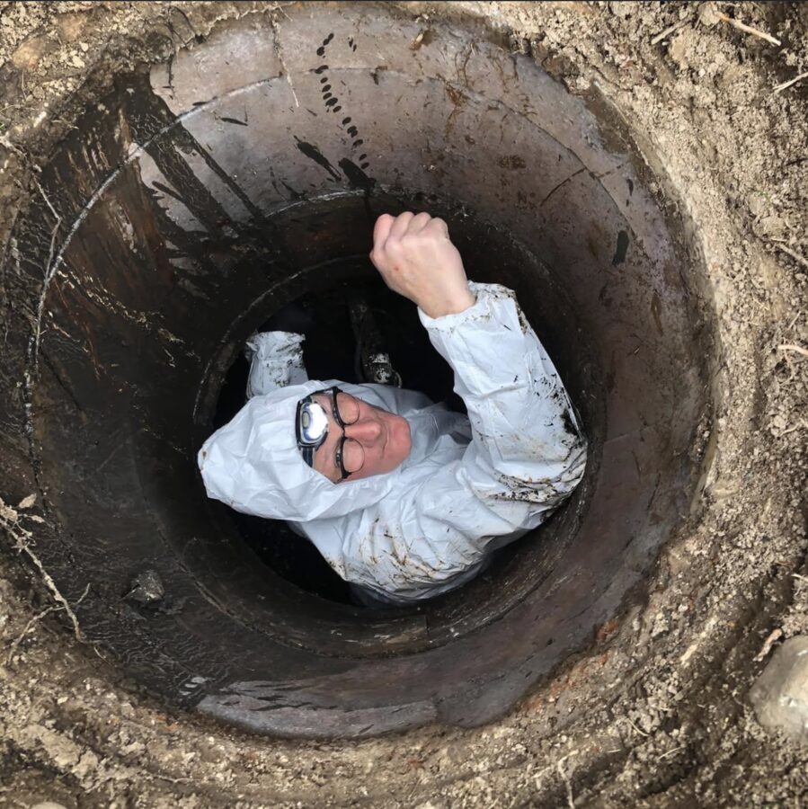 Chris down a manhole in a protective suit, fist raised